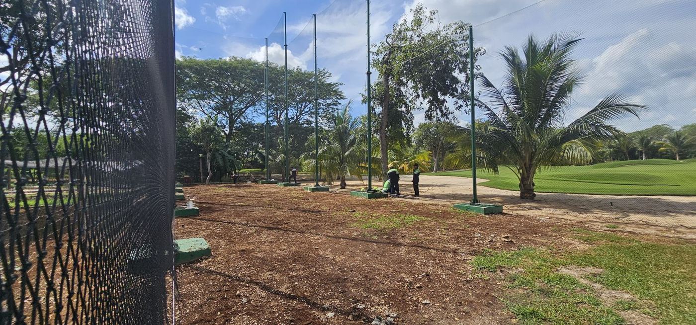 Instalación de red perimetral con postes verdes junto a un campo de golf