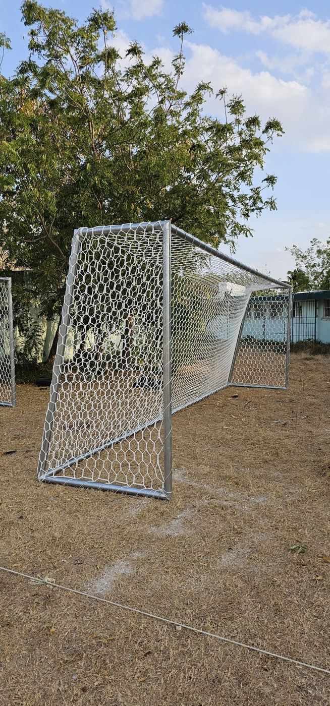 Portería de fútbol galvanizada con red hexagonal blanca en un campo de juego