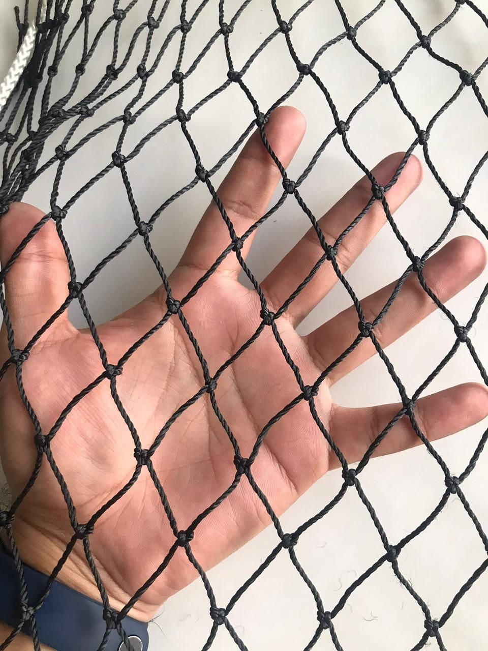 Mano detrás de una red de nylon negra que muestra el tamaño de la malla en rombo