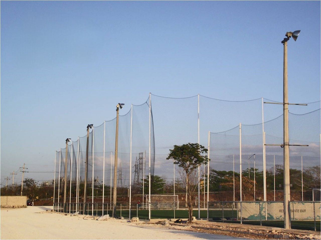 Red perimetral alta con postes y reflectores en un complejo de canchas de fútbol